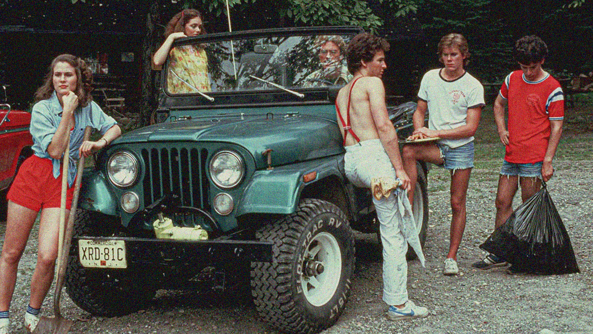 Five young men and women stand beside a Jeep on a campsite.