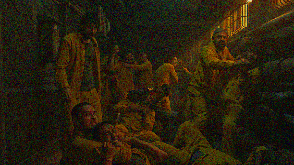A look into a darkened hallway as a bunch of inmates pause mid-brawl to look towards the camera.