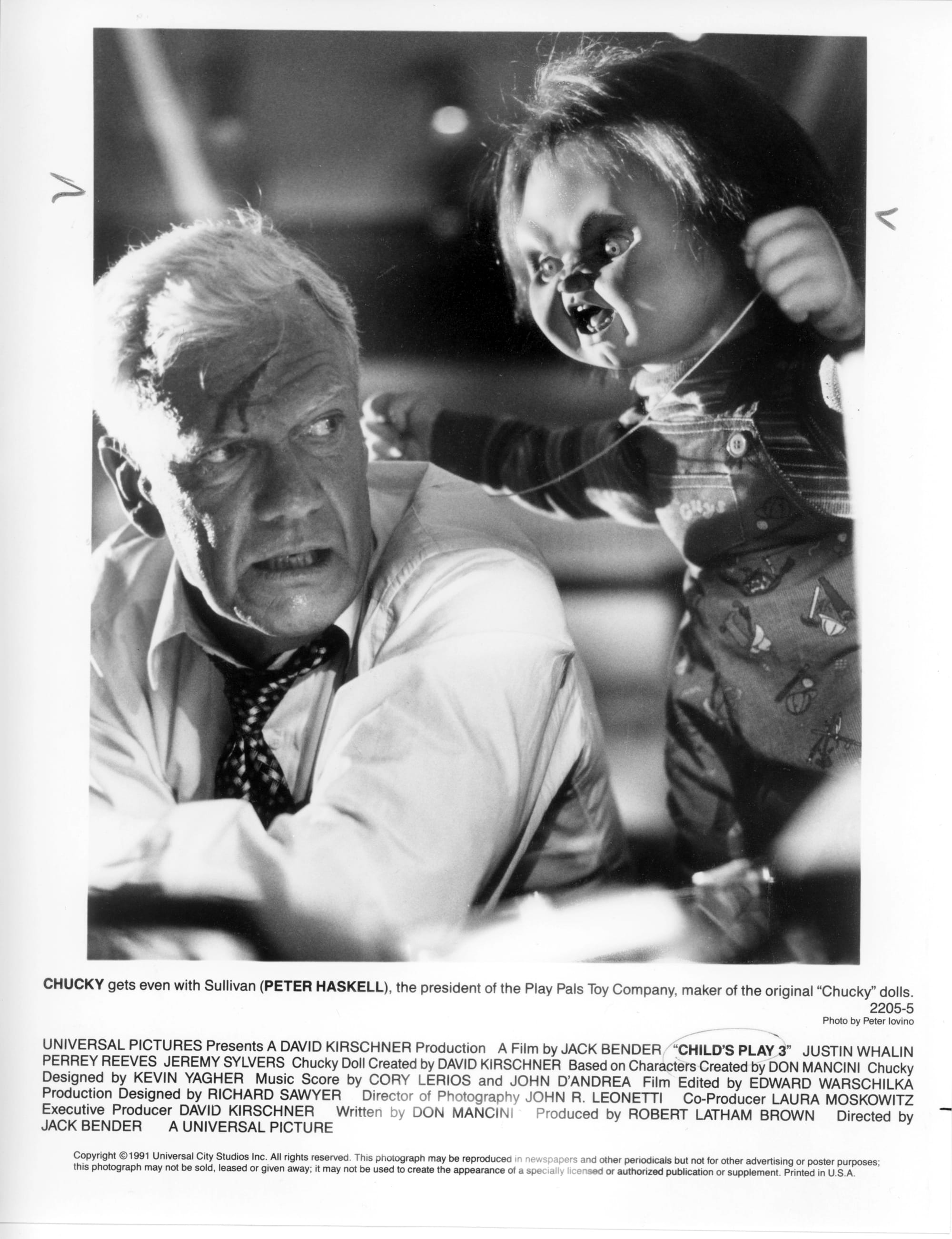 Image of an older man with blood on his forehead cowering as a doll stands over him menacingly with string in his hand.
