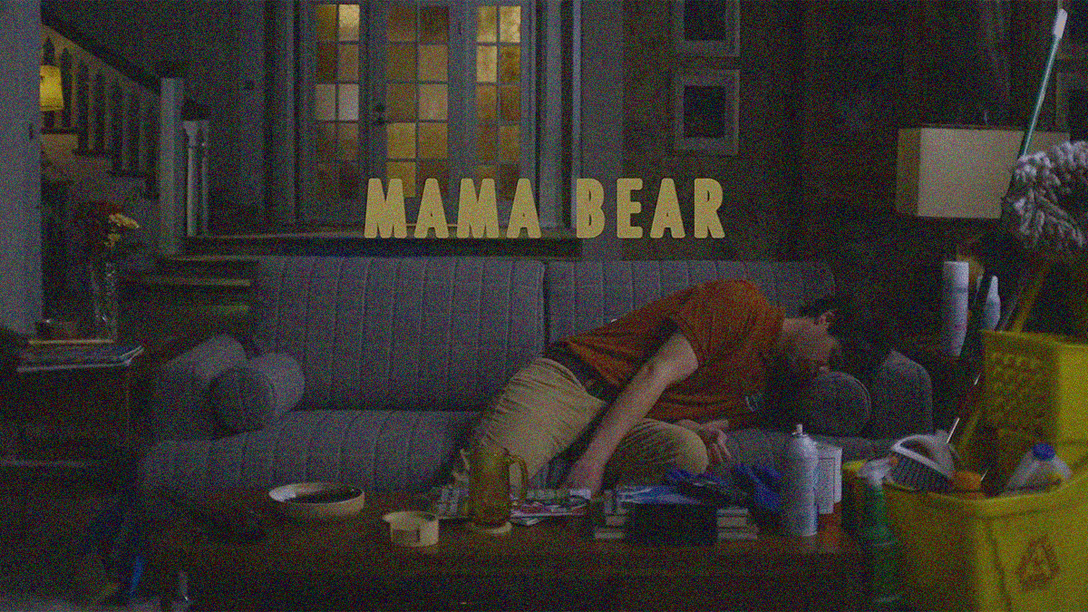 A man is flopped over and asleep on a couch. A mop bucket is seen at right.