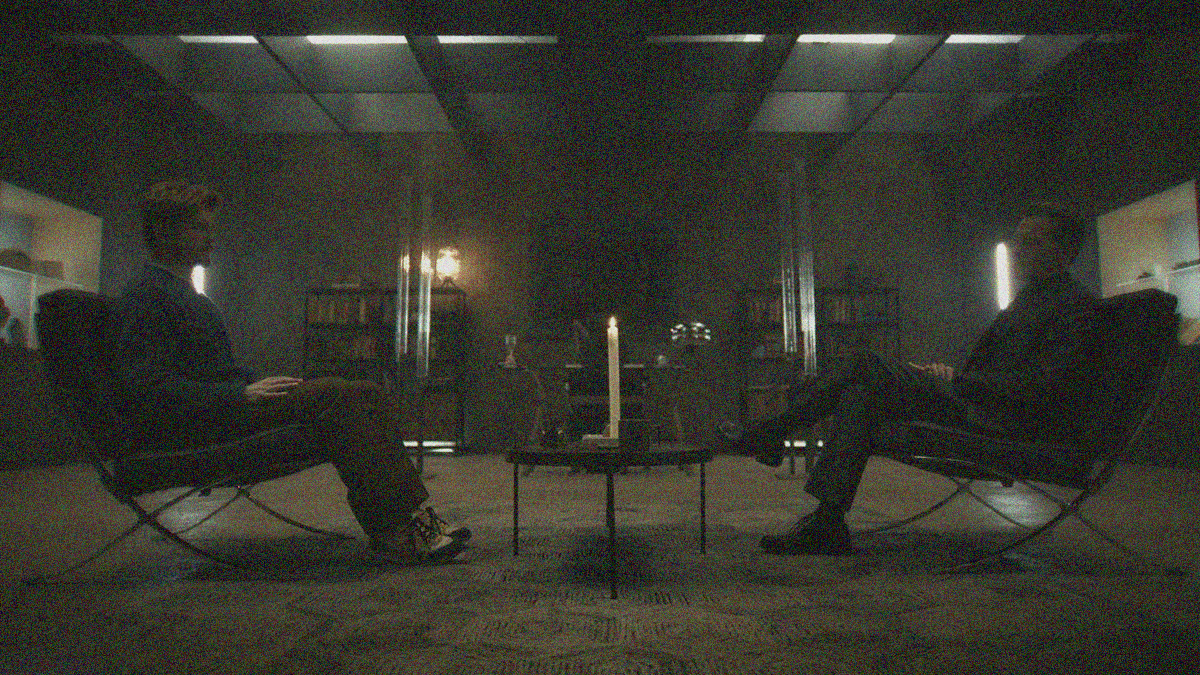 Two men sit opposite each other with a small table that holds a lit candle between them