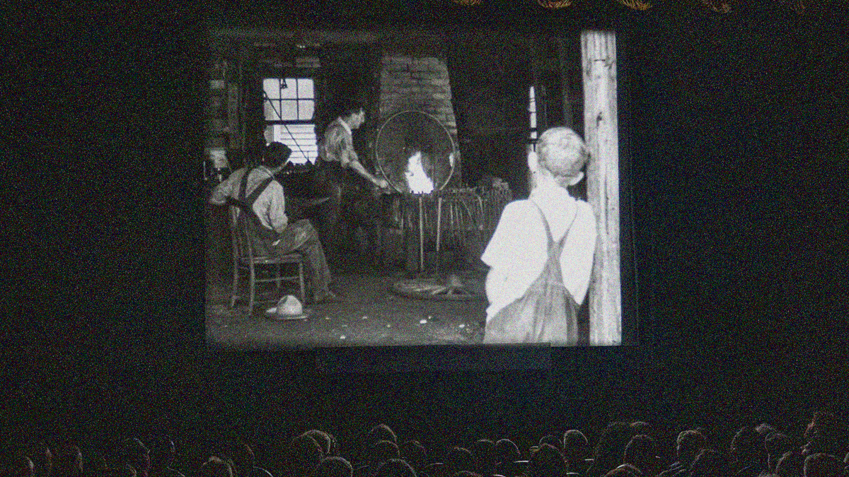 A nitrate film plays on-screen in the darkened Dryden Theatre. Audience member heads seen at bottom in seats.