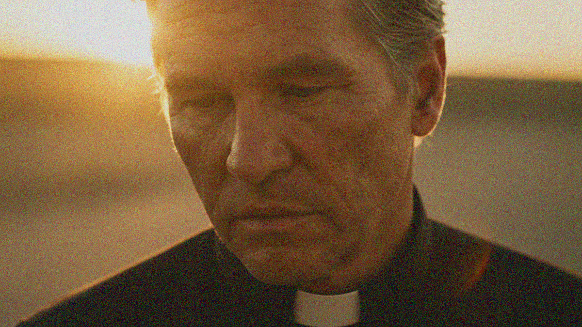 An aged priest in close-up looking downwards and forlorn as a bright sun shines behind him.
