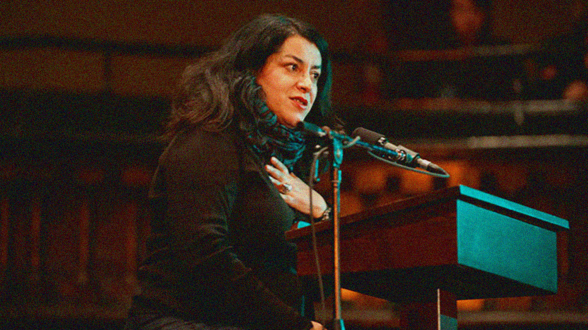 AQ woman wins on a stage behind a microphone and podium, a scarf is wrapped around her neck.