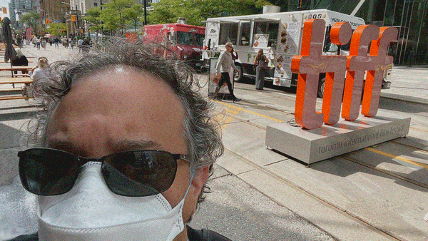 Selfie of me in sunglasses and an N95 with the TIFF logo street monument above my right shoulder.