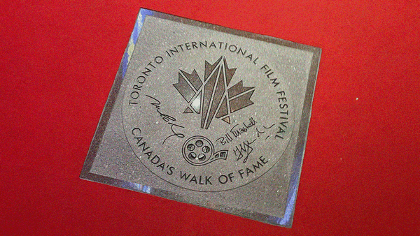 Stone plaque surrounded by red carpet. Has a geometrically broken maple leaf in center above a film reel.