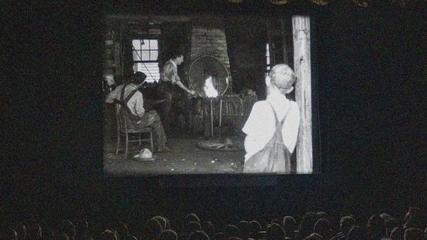 A nitrate film plays on-screen in the darkened Dryden Theatre. Audience member heads seen at bottom in seats.