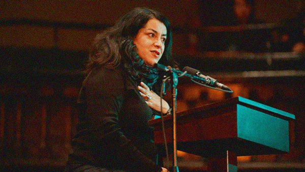 AQ woman wins on a stage behind a microphone and podium, a scarf is wrapped around her neck.
