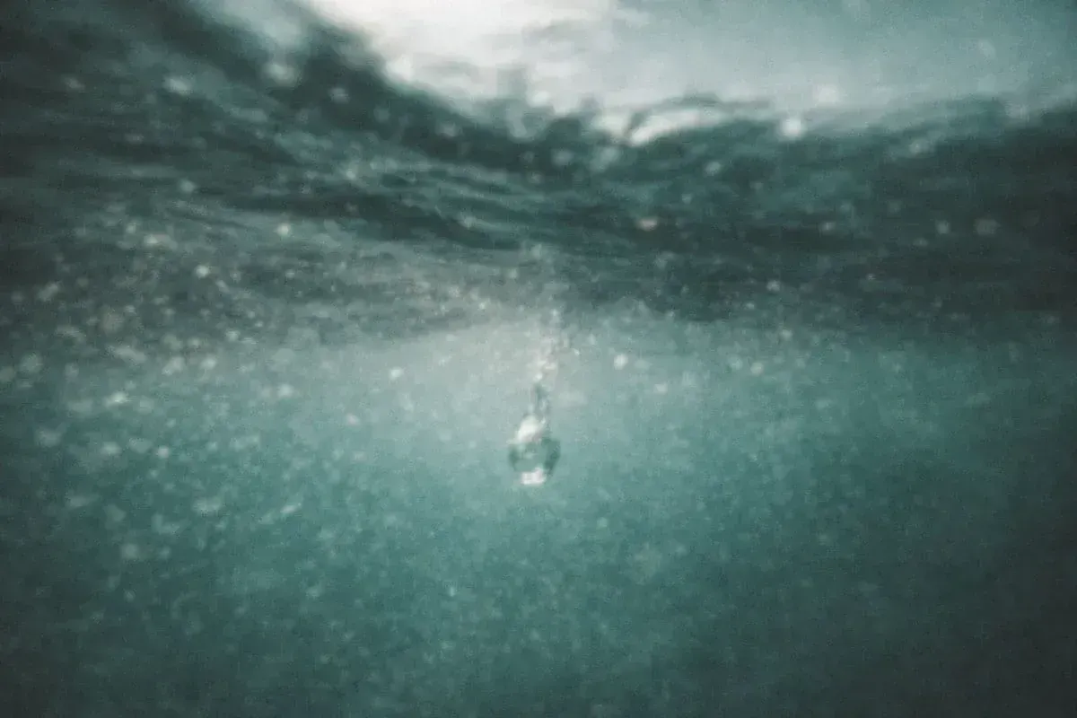 A macro photo of a single water droplet hitting a calm surface, creating perfect concentric ripples that symbolize the expansion of Divine Light. | Teachings from Khawaja Shamsuddin Azeemi.