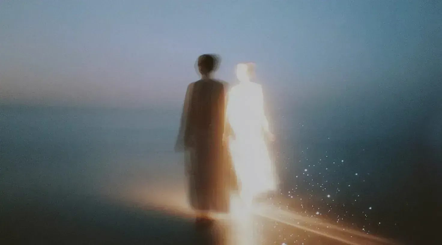 Soft-focus scene of a figure on a shoreline at dusk, one dark, one glowing white with sparkles, walking toward the horizon. | Teachings from Khawaja Shamsuddin Azeemi.