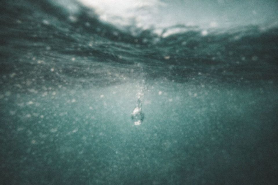 A macro photo of a single water droplet hitting a calm surface, creating perfect concentric ripples that symbolize the expansion of Divine Light. | Teachings from Khawaja Shamsuddin Azeemi.