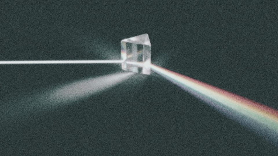 A glass prism refracting a beam of white light into a rainbow spectrum against a dark grey background. | Teachings from Khawajah Shamsuddin Azeemi (RA).