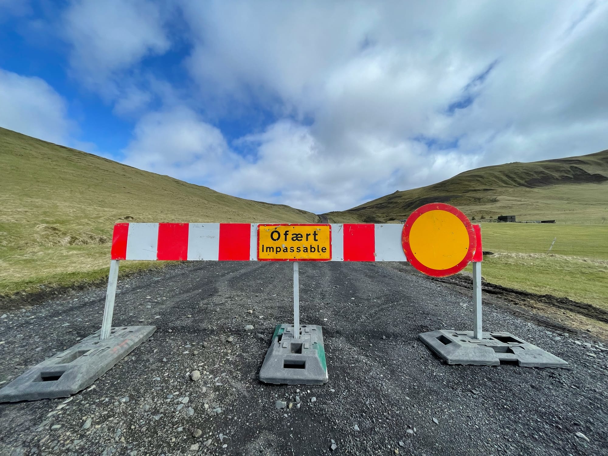 'Impassable Road' barrier on a deserted road with a partly cloudy sky above