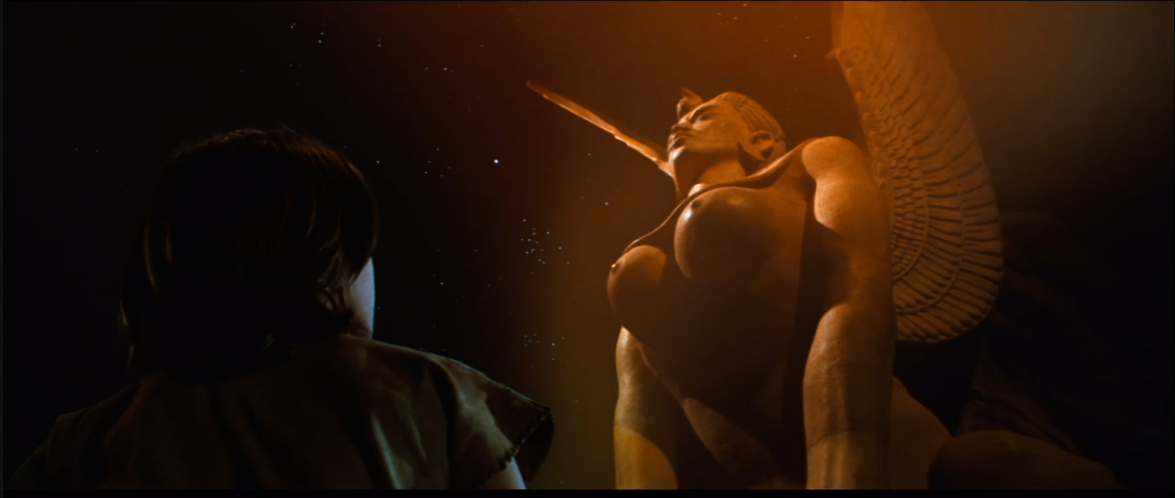 Screengrab showing a huge winged statue that also happens to be topless.