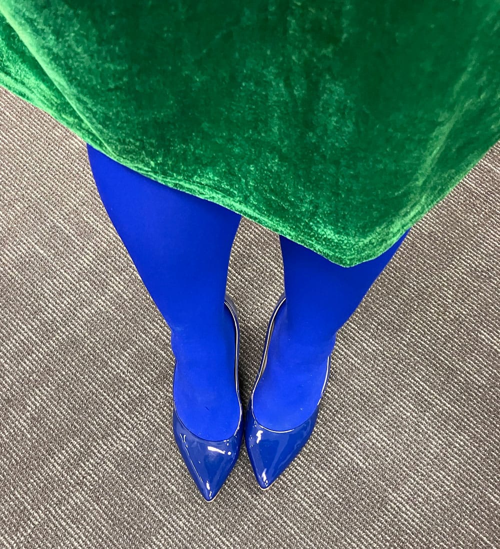 Looking down on legs in electric blue tights, blue patent leather heels, and a kelly green dress.