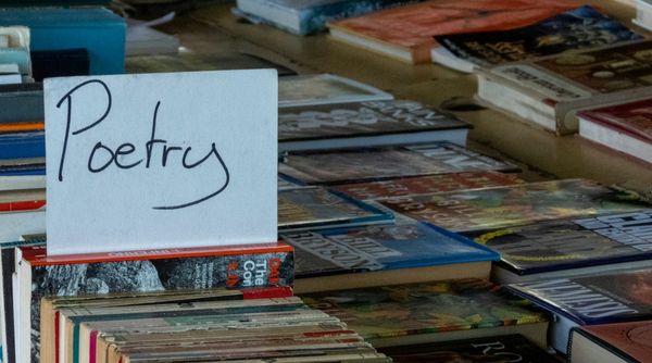 Photo of rows of secondhand books. There is a cardboard sign that says "Poetry" poking up between two of them.