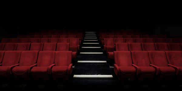 A movie theatre looking at rows of red seats with an aisle running through the middle. They are all empty.