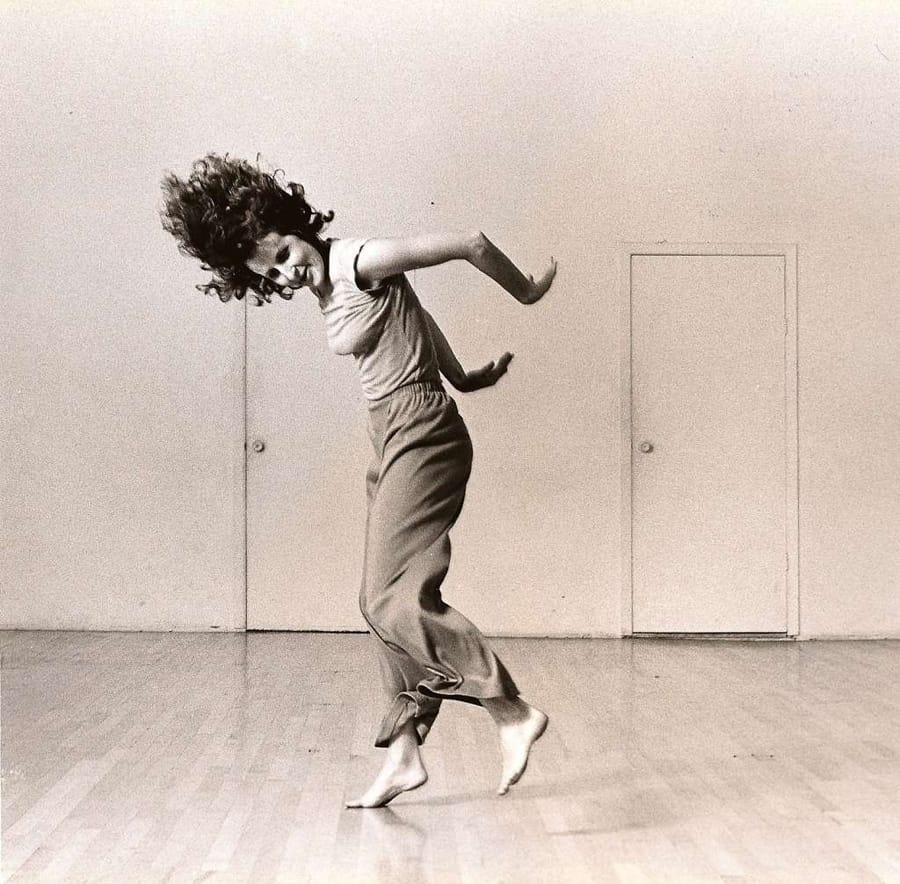 Trisha Brown is in motion, arms tossed behind her, hair suspended, one foot hovering and the other barely on the ground