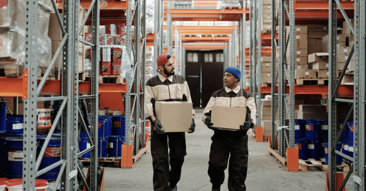 Two warehouse workers talking together holding boxes.