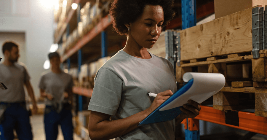 A warehouse worker holding a pad writing inventory.
