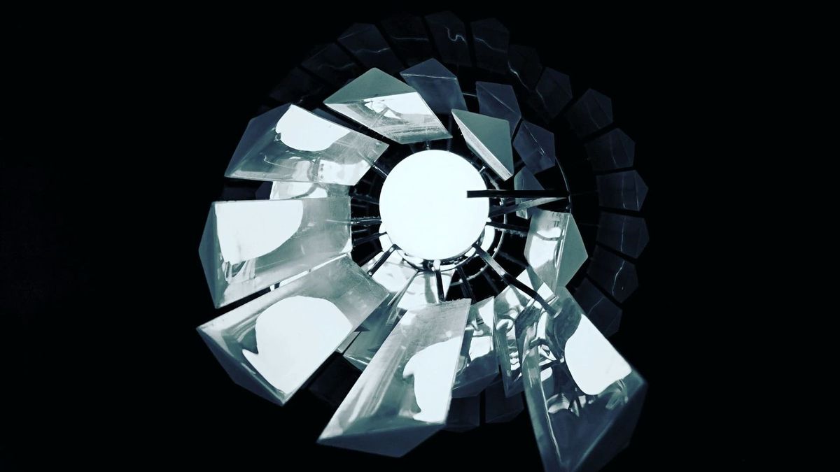 "Minimalist, high-contrast overhead photograph of a fractured geometric light fixture with metallic shards surrounding a bright central ring of light."