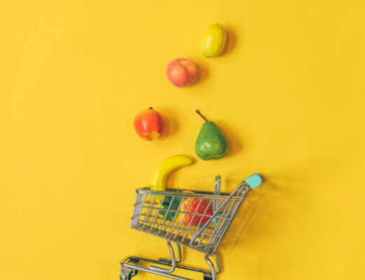 Grocery cart with fruit coming out of it on a yellow background