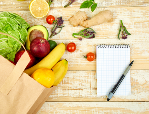 A notepad on a wooden table with a bag of produce.