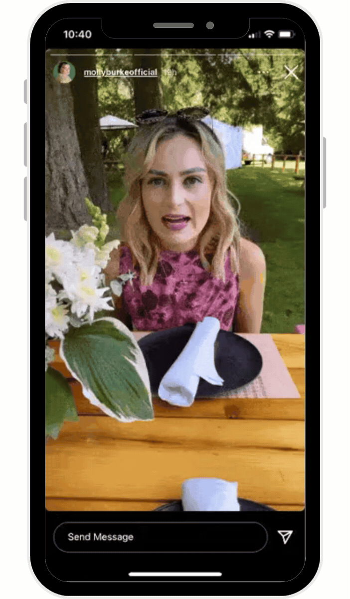 Woman seated at an outdoor table with flowers, viewed inside a smartphone frame displaying instagram stories, showing a casual lifestyle moment shared on the app.