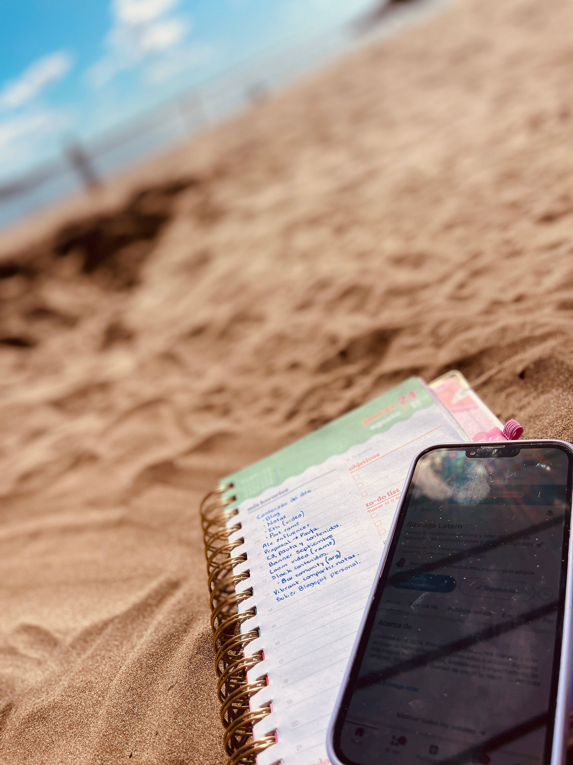 Foto de un Cuaderno y un Celular en la arena de la playa