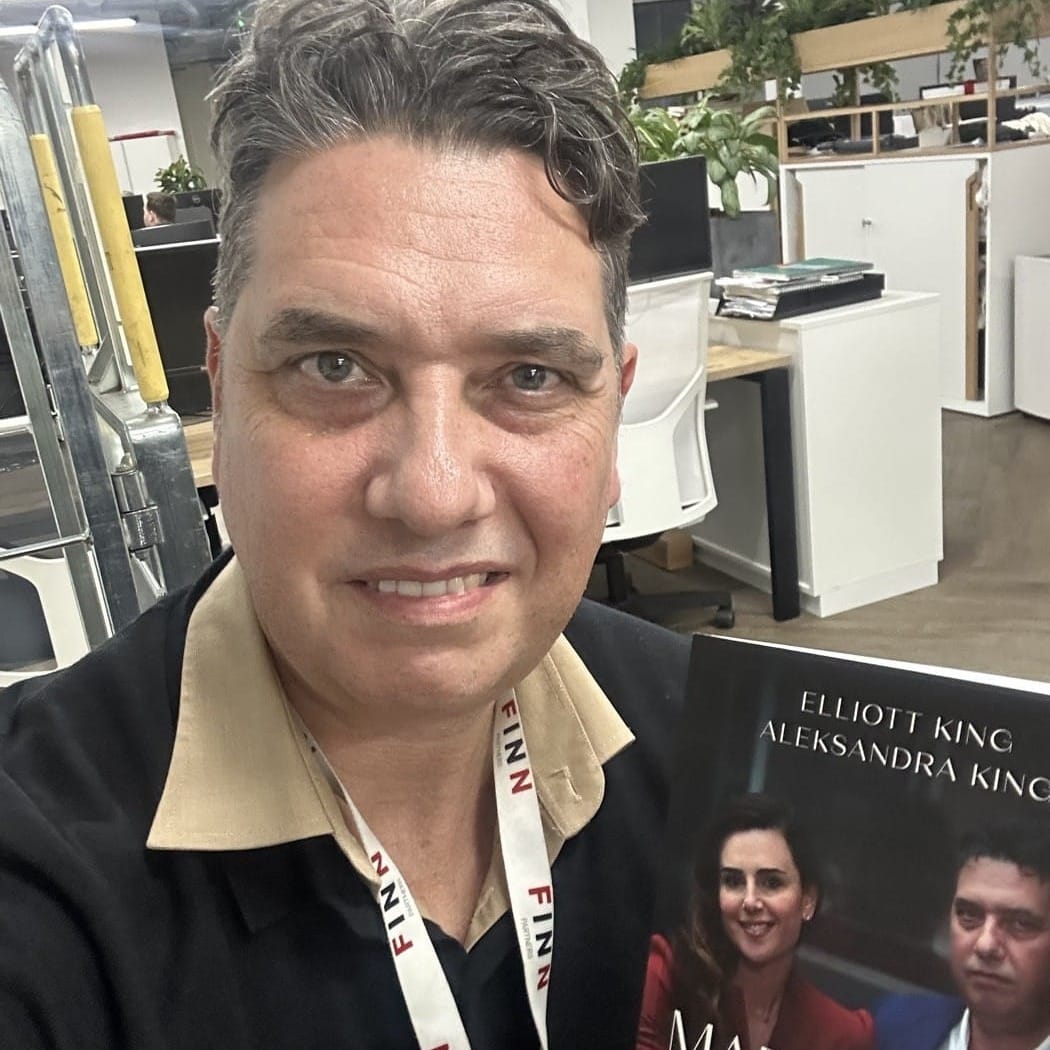 Elliott King holding a copy of Marketing Wins, the book he co-wrote with Aleksandra King, in an open-plan office and wearing a FINN Partners lanyard.