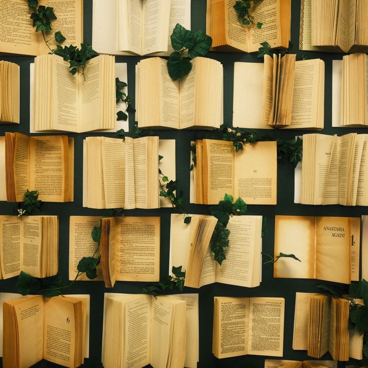 A wall covered in open, yellowing paperback books with vines curling around them