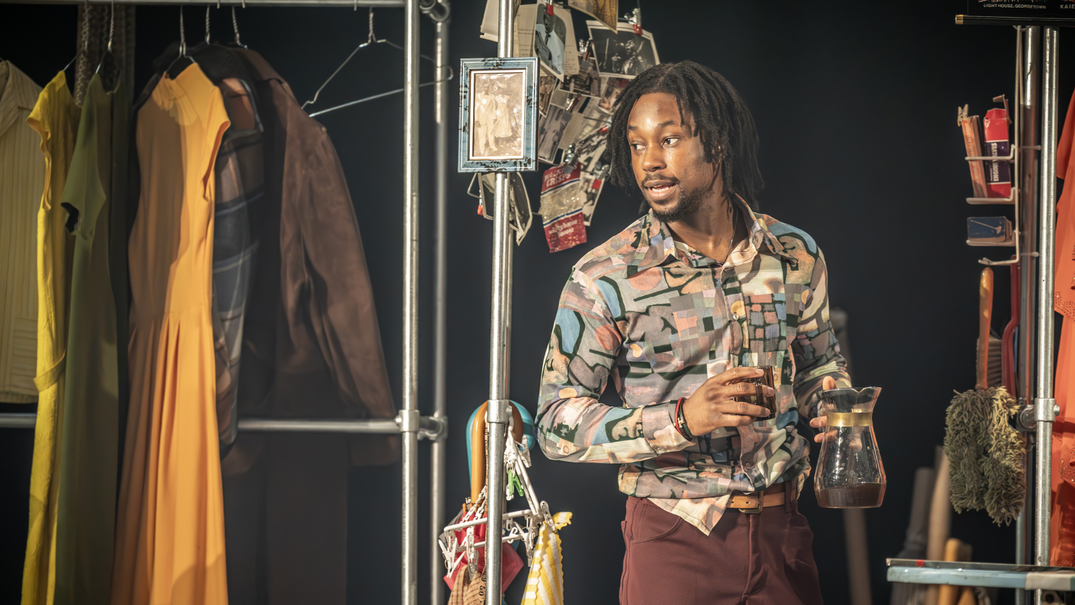Alterations star Raphel Famotibe holding jug in coloured print shirt on stage at The National Theatre