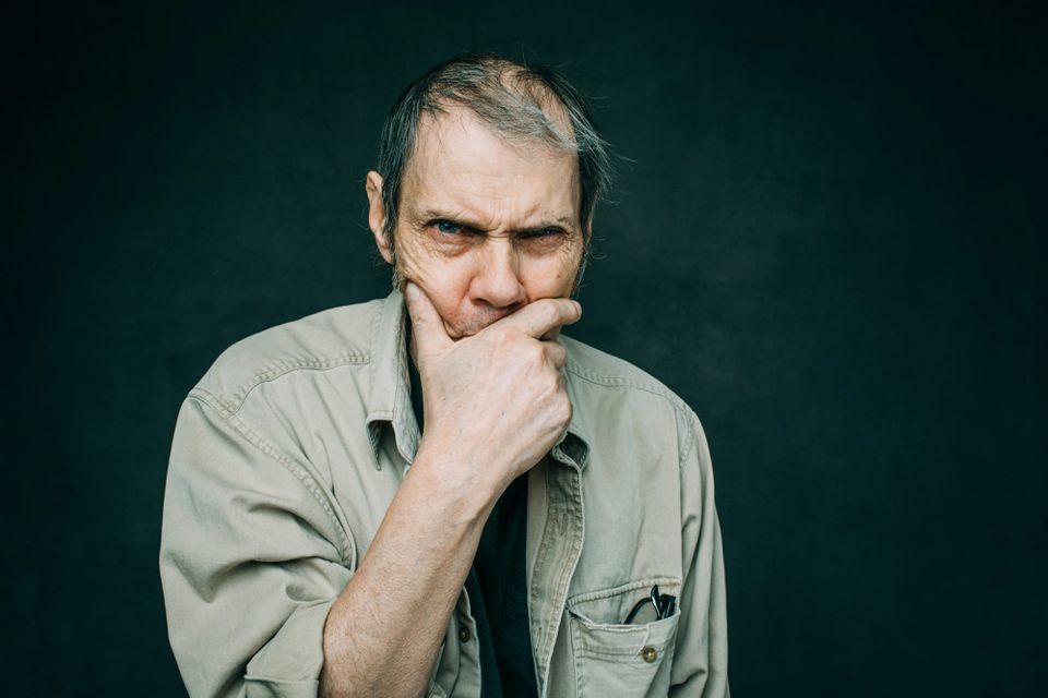 Malcolm Holcomb stares intently into the camera, covering his mouth with his hand.