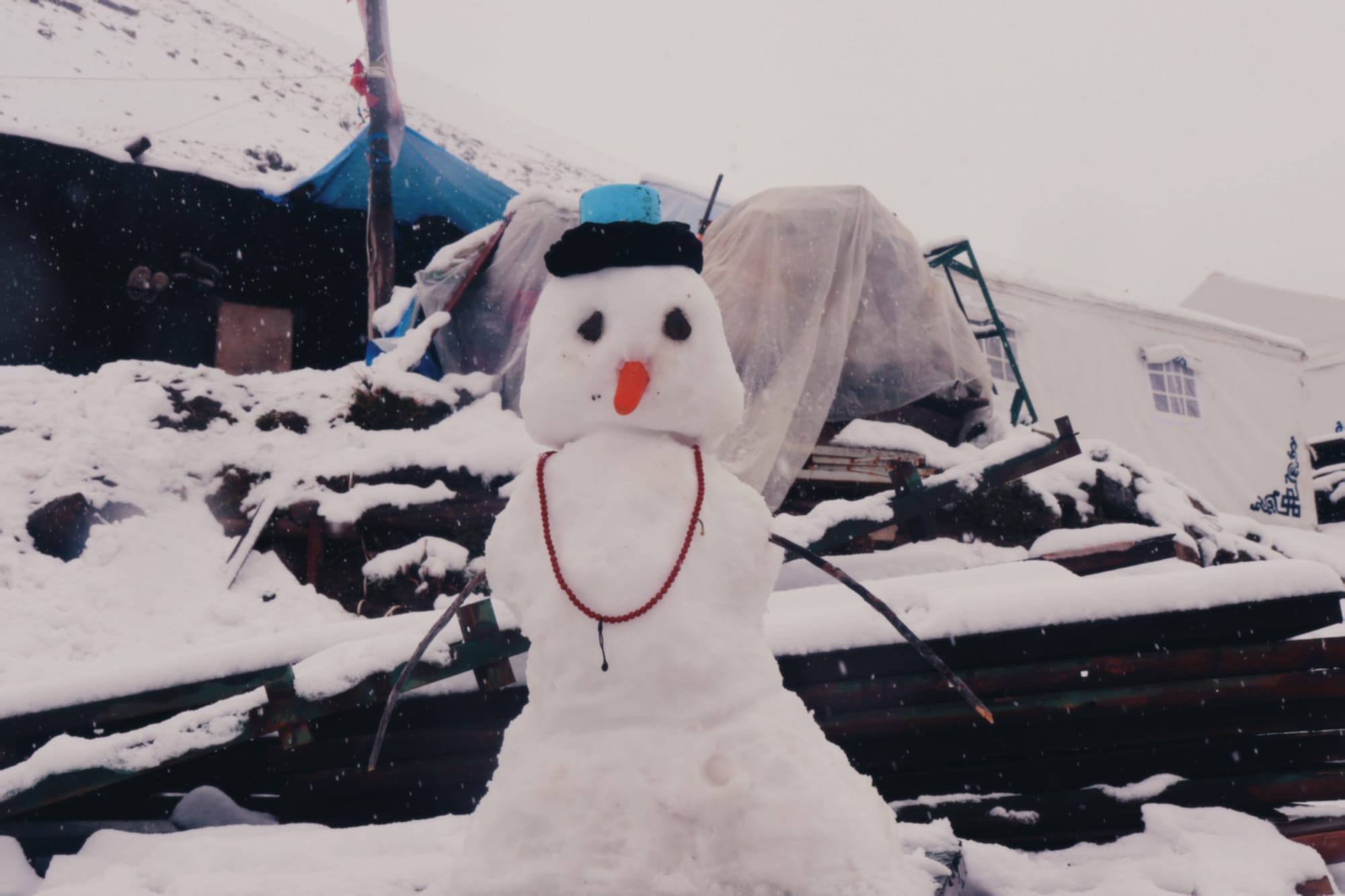a snow person wearing rosary, a hat, and a long orange nose