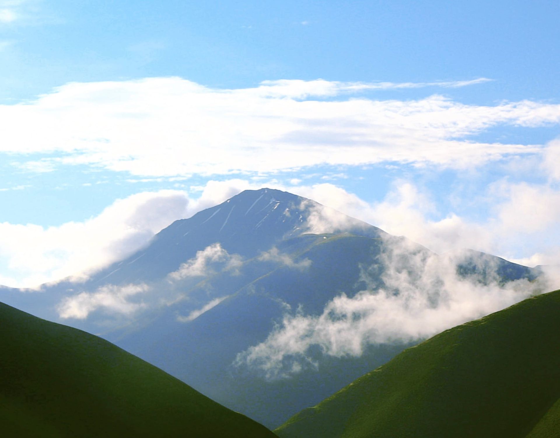 a mountain stands in the midst of cloud and fog against blue sky