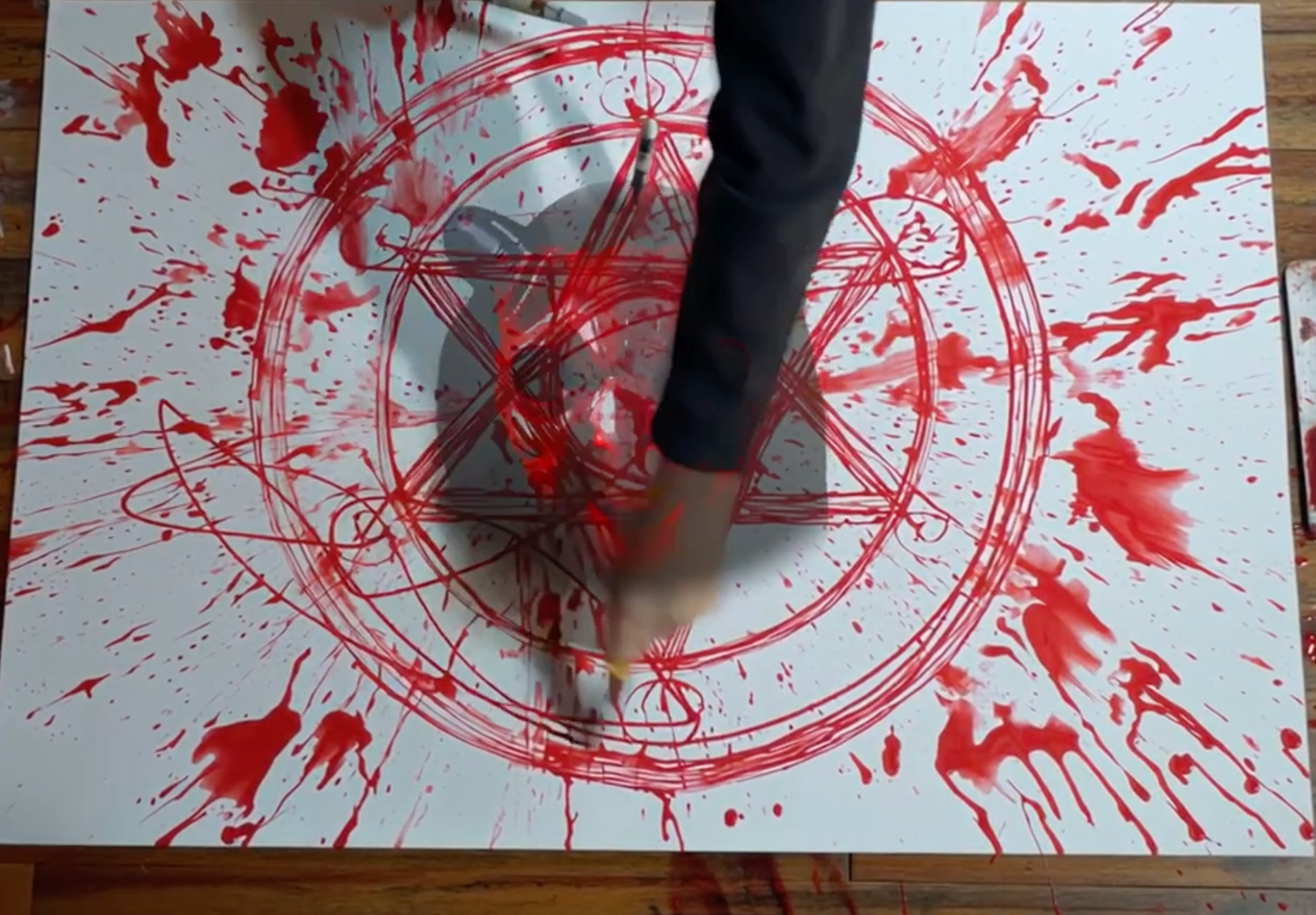 A Childs arm paints a star with a circle in red. The center of the circle has demon face in it.