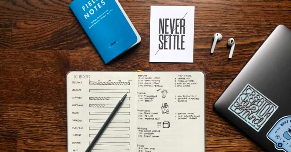 A desk with various items on it, including two notebooks, a MacBook and a pair of AirPods.