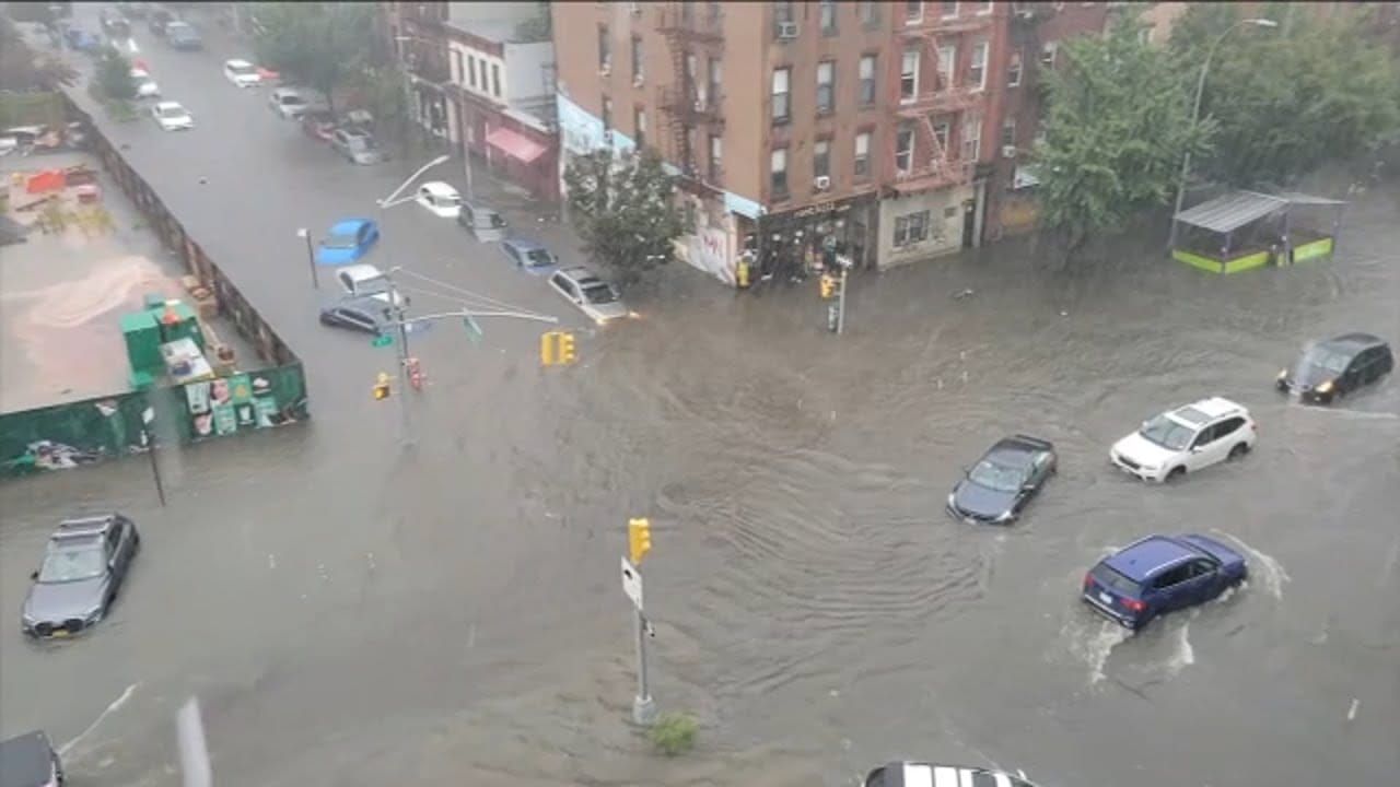 New York City streets underwater during severe flooding with cars surrounded by water.