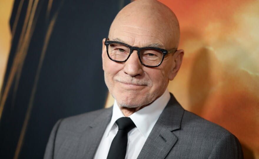 Sir Patrick Stewart attending an event, looking distinguished in a blazer, with promotional imagery of his roles as Professor X and Captain Jean-Luc Picard.