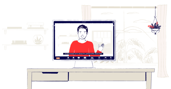 A computer screen on a desk showing a webinar. A man wearing a read sweater is speaking, with live captions.