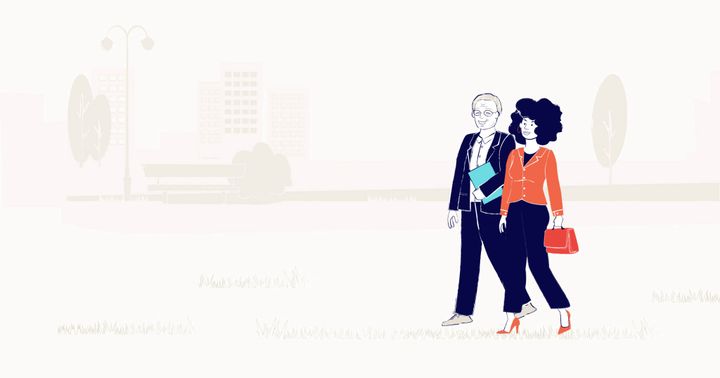 A man and a woman dressed in business attire walk in a park together