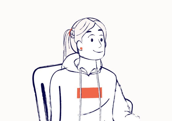 A young woman sitting on an office chair. She has her hair tied up and is wearing a hoody and red earrings.