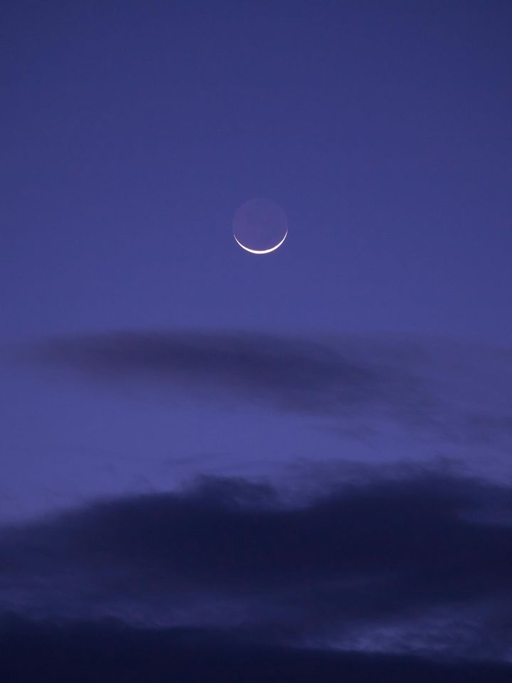 waxing crescent moon tipped up like horns, bright in a cloudy purple sky
