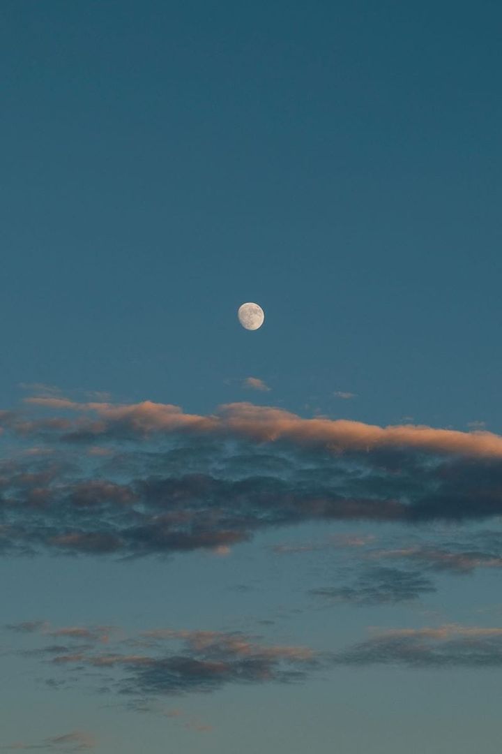 waxing gibbous moon in a vast sky at dusk, with streaks of stratus clouds below