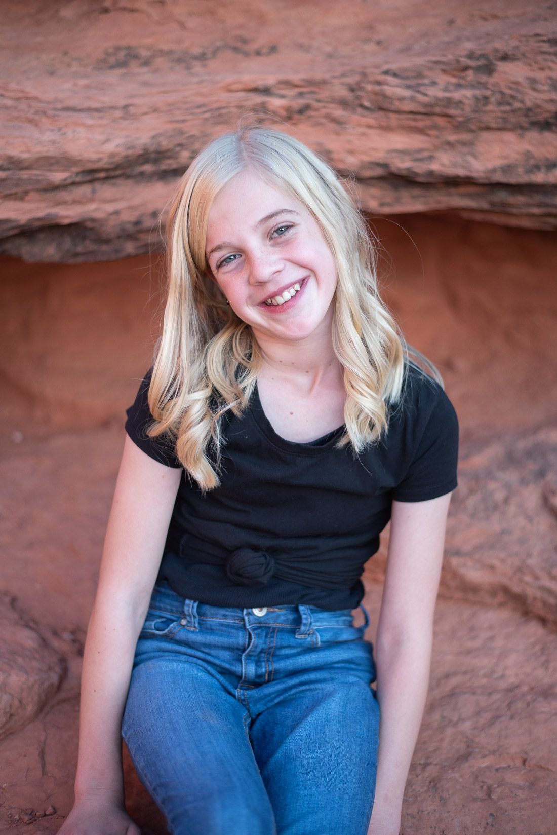Girl sitting on red rocks and smiling at the camera
