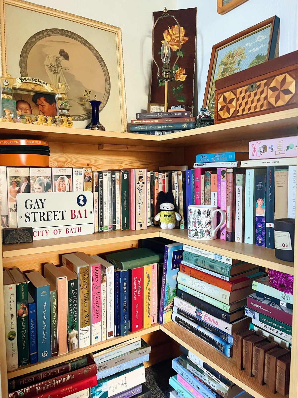 A corner bookshelf with dozens of copies of Jane Austen novels and Austen-related books. There are also knick knacks.
