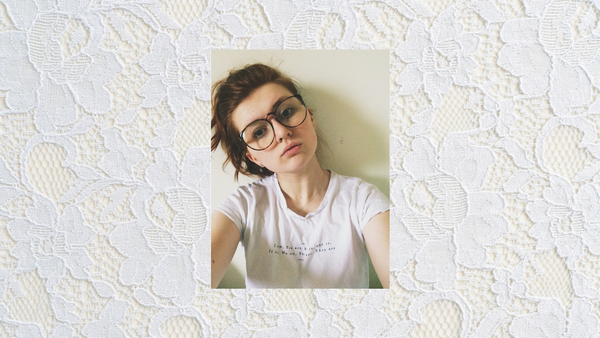 A redheaded person pouts in a selfie, standing against a plain white wall. Their shirt reads 'I am, you are, he is, she is, it is, we are, you are, they are'