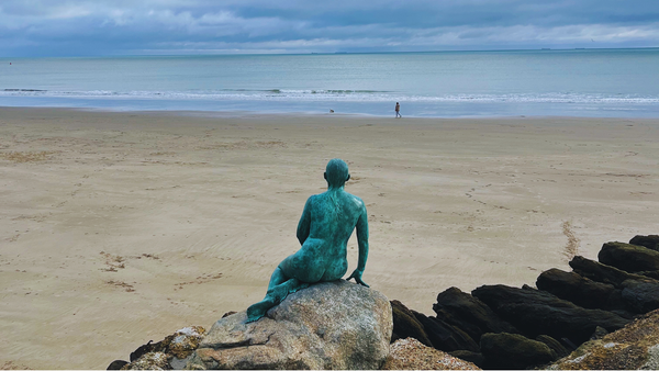 A photo from behind the Folkestone mermaid statue, and patinated bronze sculpture of a nude woman. It sits on a rock, facing towards the sea on Sunny Sands in Folkestone, England. 