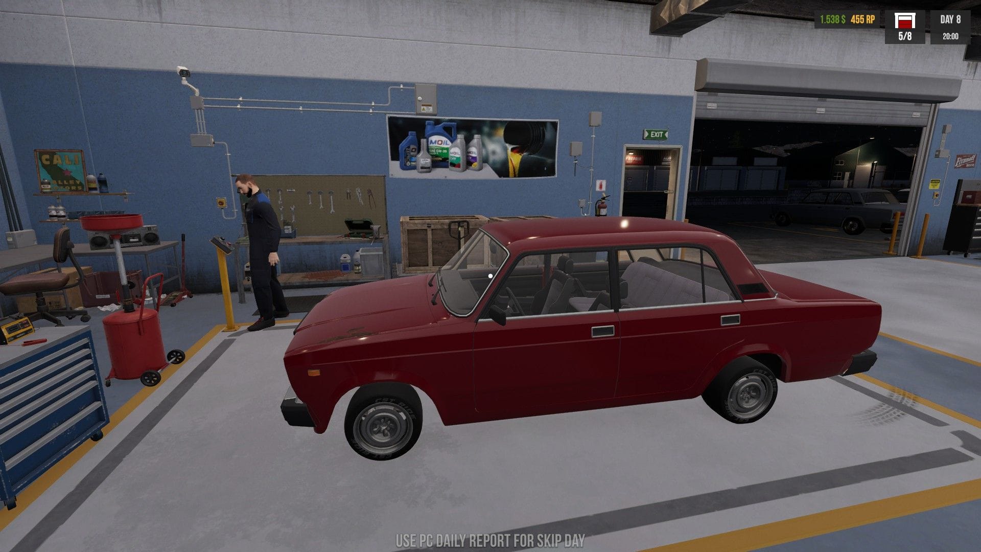 A red car awaits service on the floor of the garage as Jonty's character inspects a button.