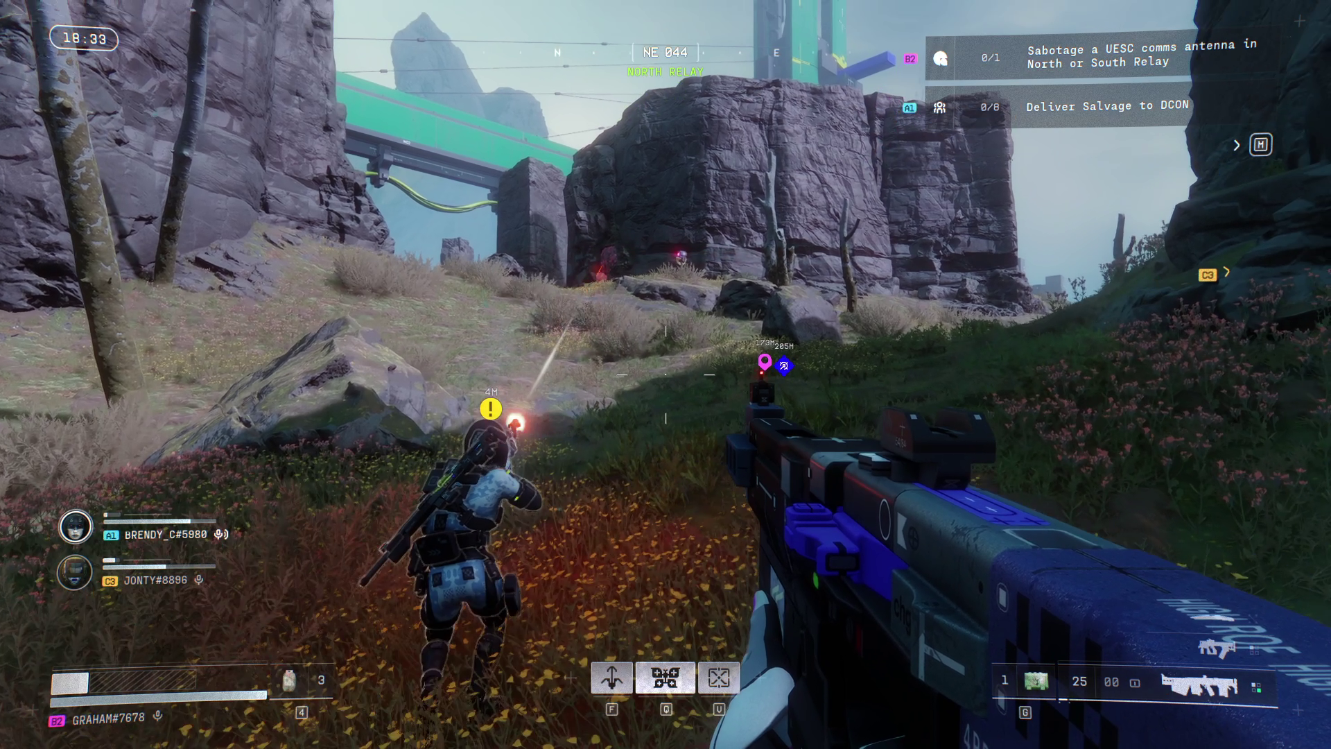 The players in a field shoot at a distant robot or turret, next to some grey rocks.